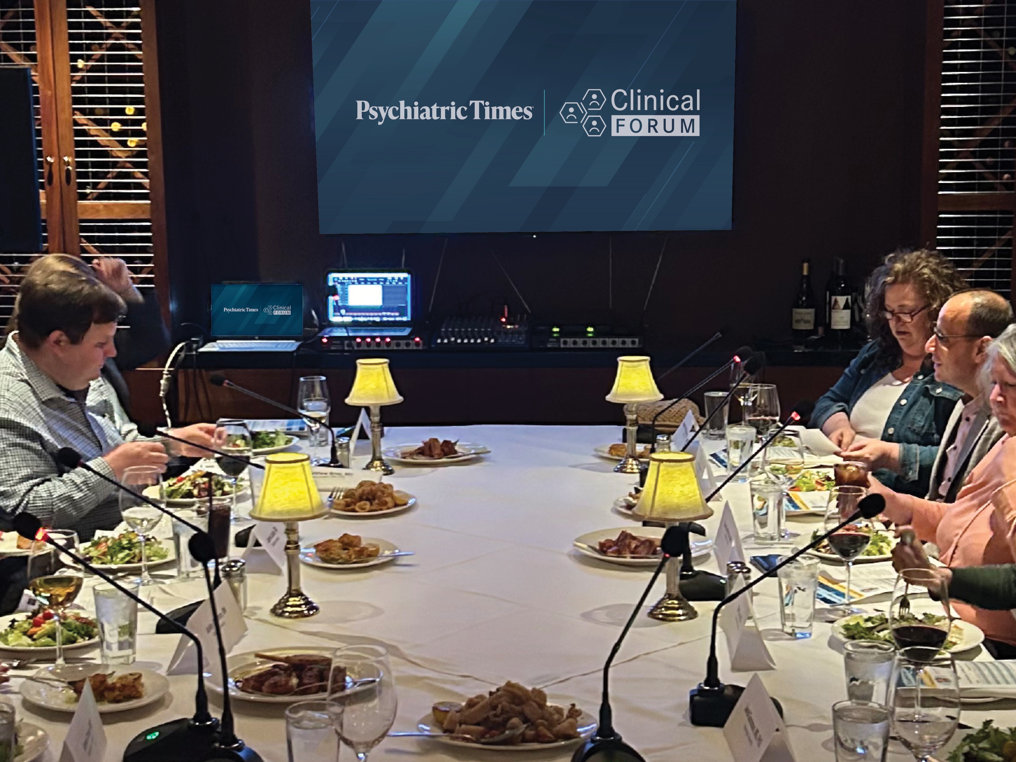 A dinner event setup with attendees discussing psychiatric treatment approaches.