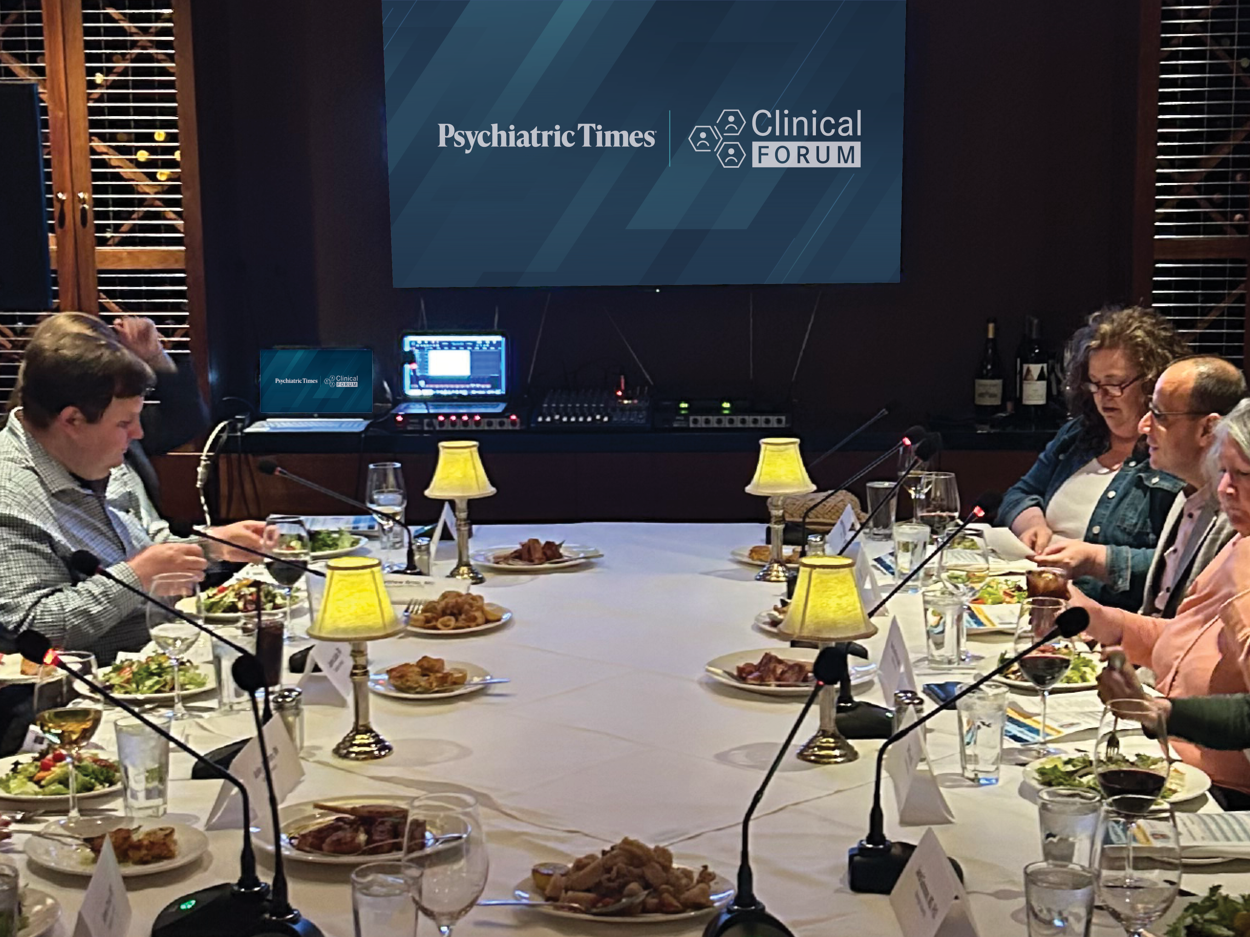 A large, elegant private dining room with several tables arranged. Guests are seated, engaged in conversation about psychiatric treatment approaches.